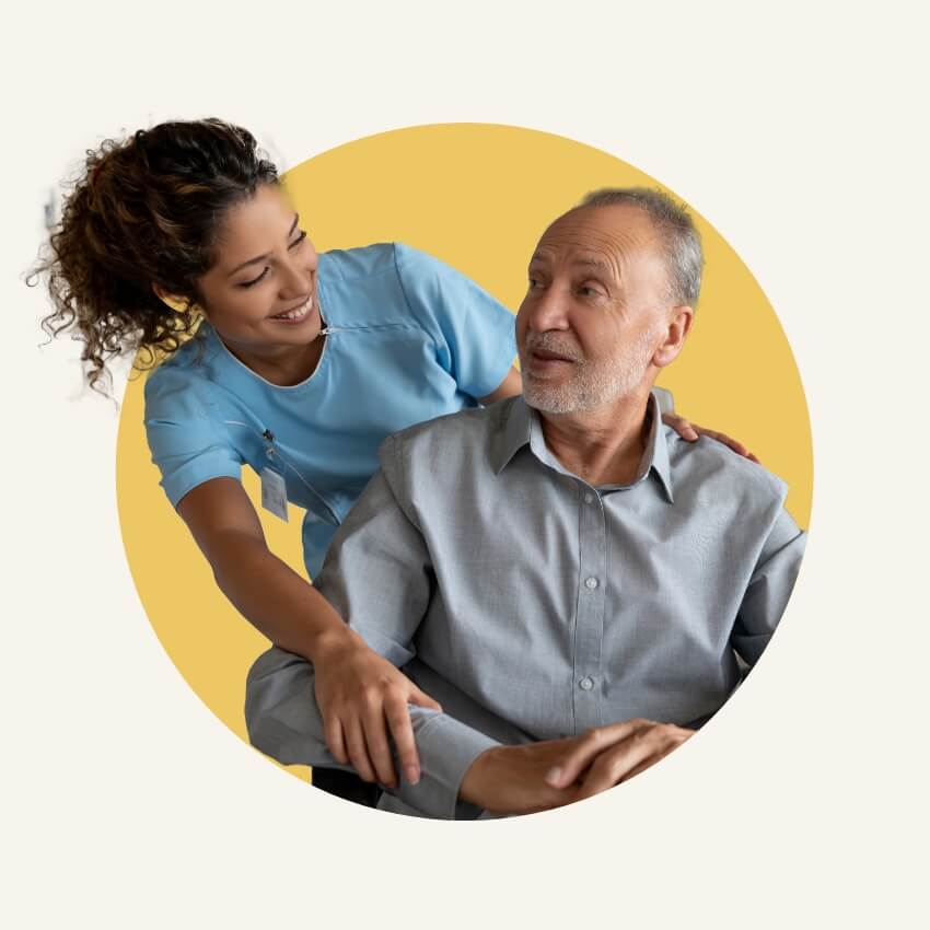 Smiling caregiver in blue scrubs supporting an elderly man, representing Advanced Nursing & Home Care’s personalized and compassionate in-home care.