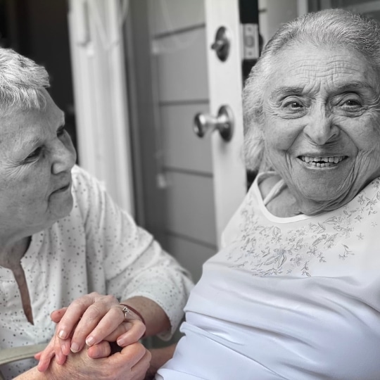 Elderly woman smiling while holding hands with her caregiver, representing compassionate and personalized home care from Advanced Nursing & Home Care.