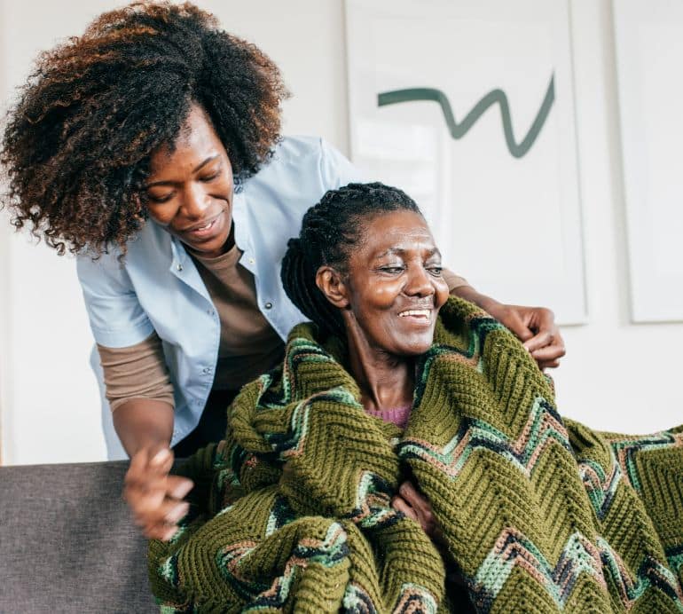 Caregiver helping an elderly woman stay comfortable with a blanket, symbolizing the compassionate in-home support from Advanced Nursing & Home Care.