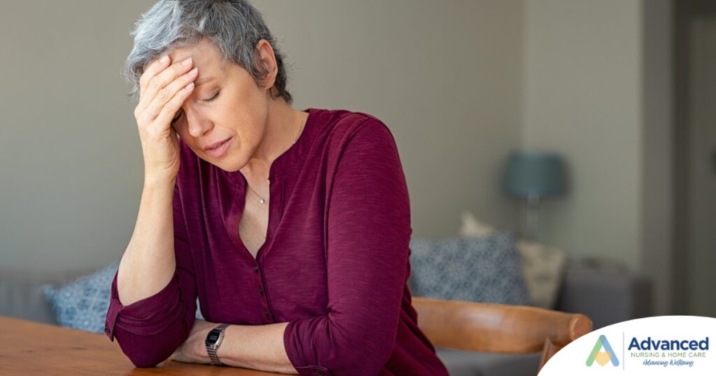 A woman holds her head in her hand, representing the stress that new family caregivers go through.