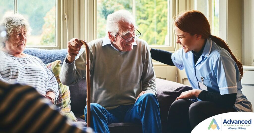 A caregiver is smiling and supporting an elderly man with a cane while another senior woman looks on, showing trust and compassionate home care.