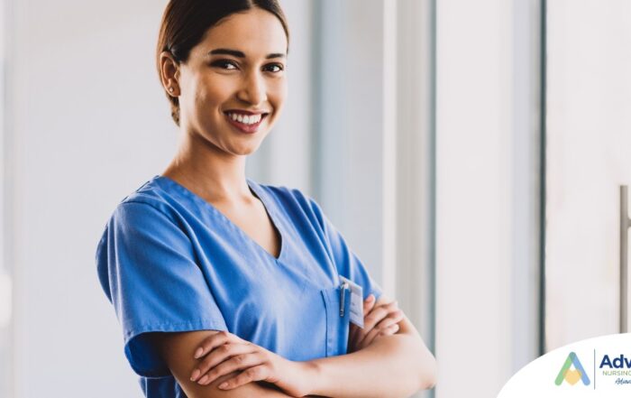A smiling caregiver in blue scrubs stands confidently with arms crossed, representing the compassionate and professional care at Advanced Nursing & Home Care.