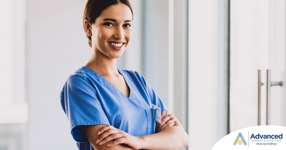 A smiling caregiver in blue scrubs stands confidently with arms crossed, representing the compassionate and professional care at Advanced Nursing & Home Care.