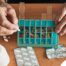 An elderly person organizes pills in a weekly medication box, representing safe and reliable medication management support from Advanced Nursing & Home Care.