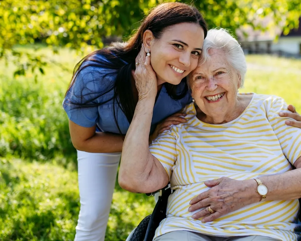 Caregiver and senior woman embracing in garden