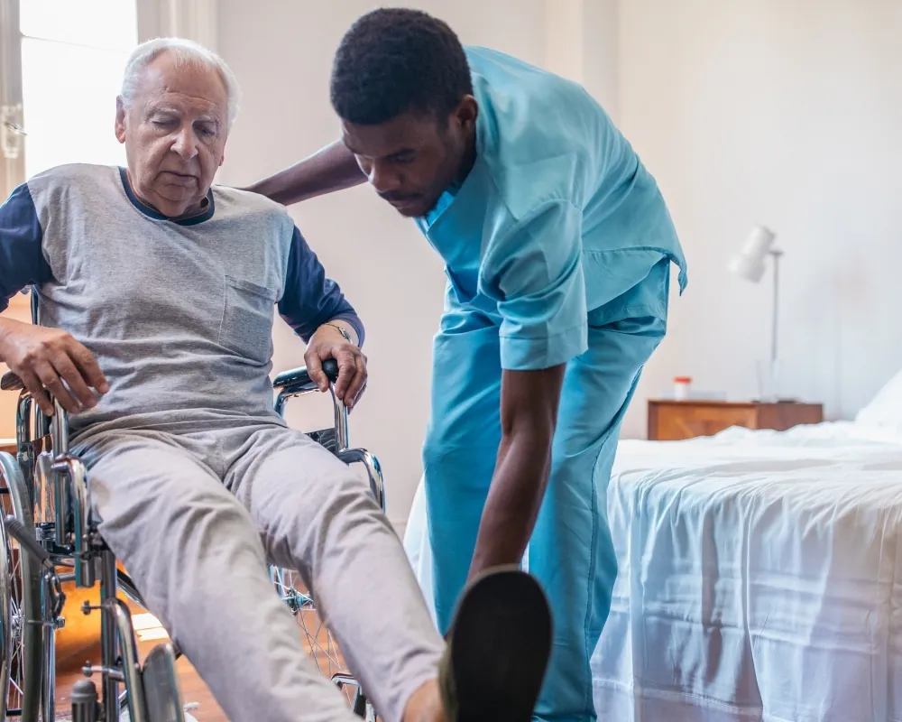 Caregiver helping senior man in wheelchair in bedroom
