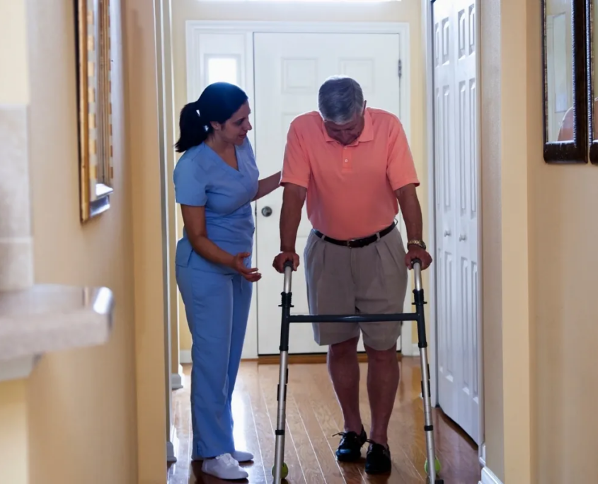 Caregiver helping senior man walk in hallway