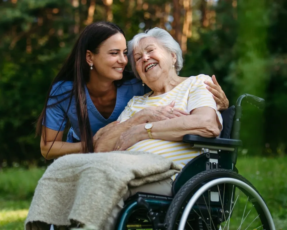 Caregiver hugging senior woman in wheelchair outdoors