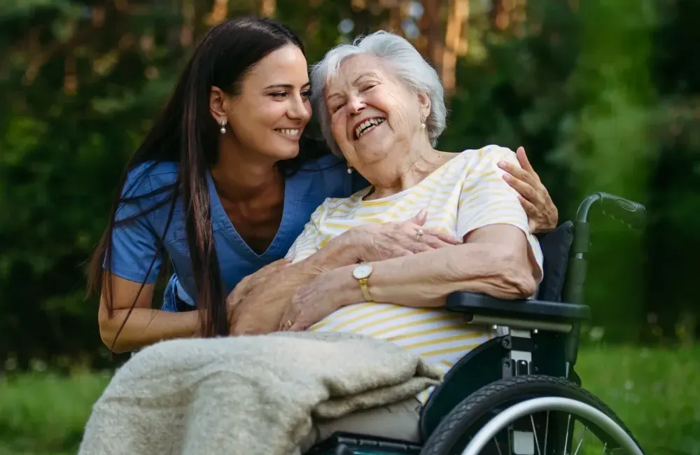Caregiver hugging senior woman in wheelchair outdoors