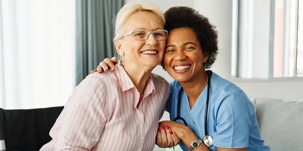 Nurse and senior woman smiling together on sofa