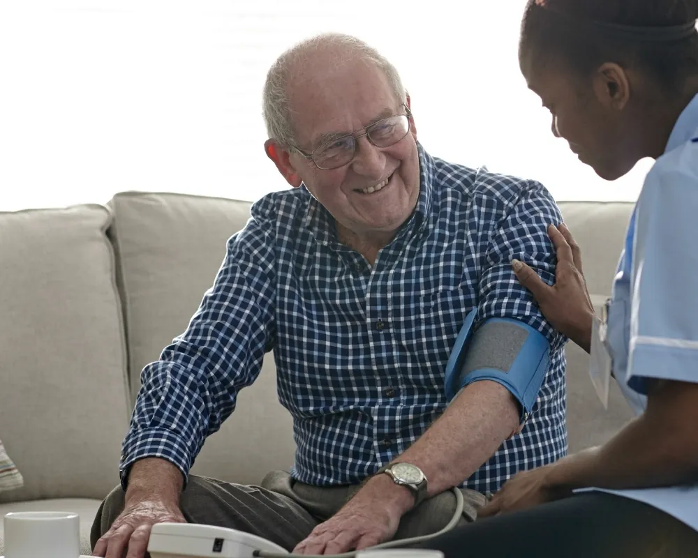 Nurse taking a senior's blood pressure on sofa