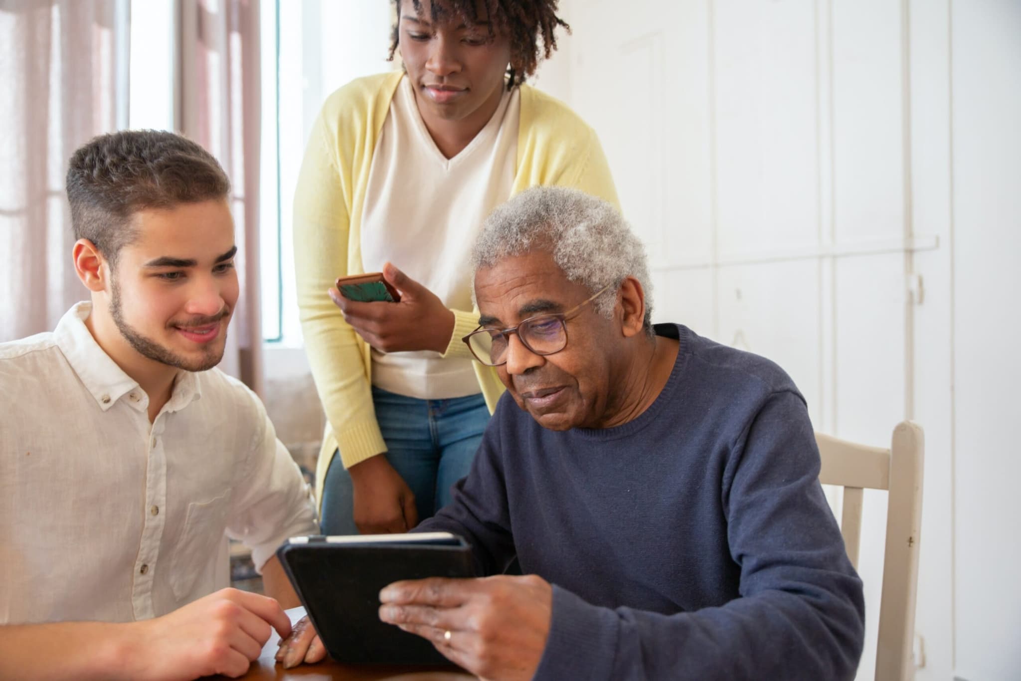 Older man using a tablet with two younger people helping him