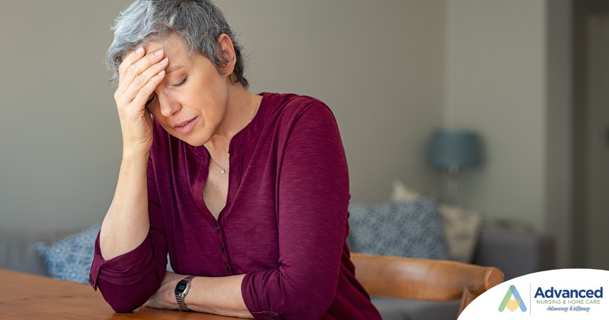 A woman holds her head in her hand, representing the stress that new family caregivers go through.