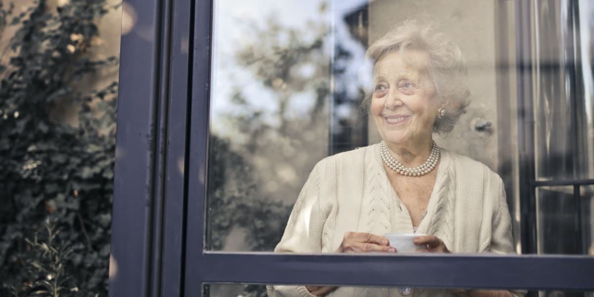 Older woman having tea and smiling looking out of a window